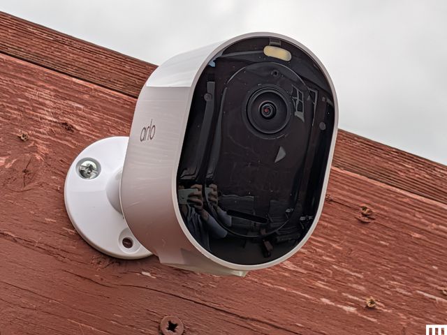 Front view of white oval-shaped security camera attached to a wooden fence